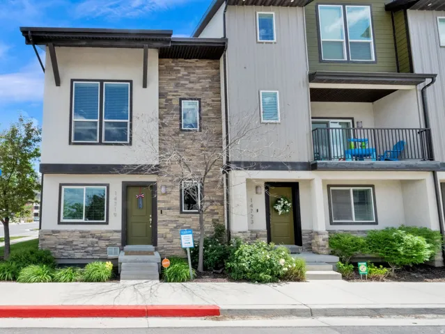 Modern townhome exterior featuring an upper-level balcony, varied siding materials, stone accents, and a landscaped front entry