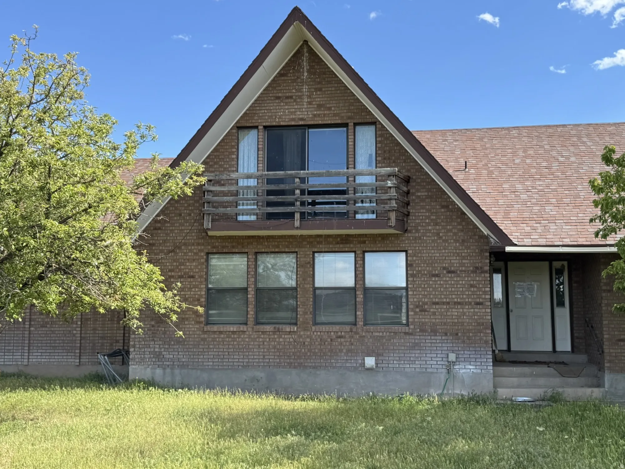 Brick facade home featuring an A-frame gable, a second-story balcony with wood railing, and a gabled shingle roof