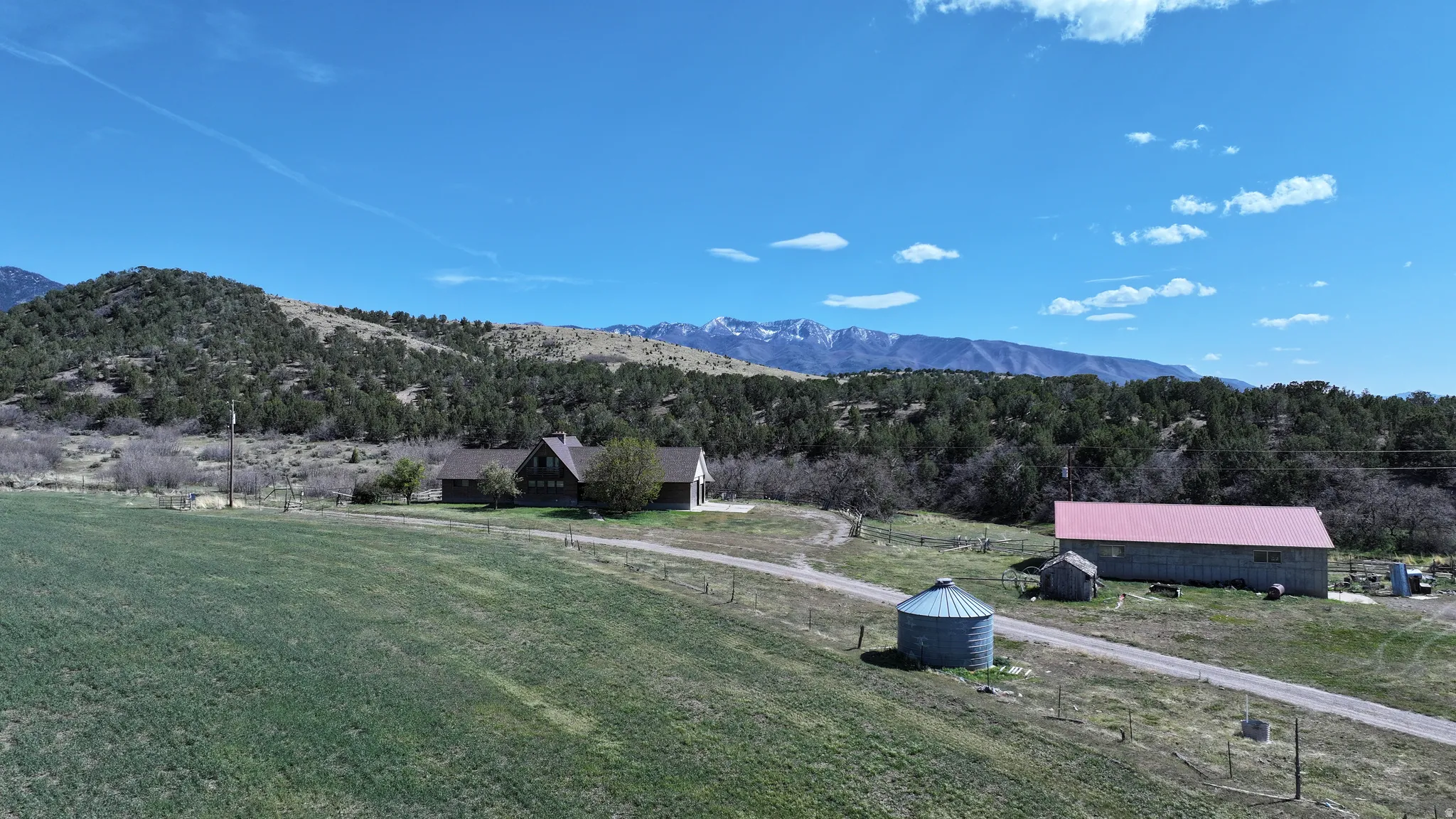 Expansive rural property featuring a main residence, a large barn with a red roof, a separate outbuilding, a grain silo, and a gravel driveway
