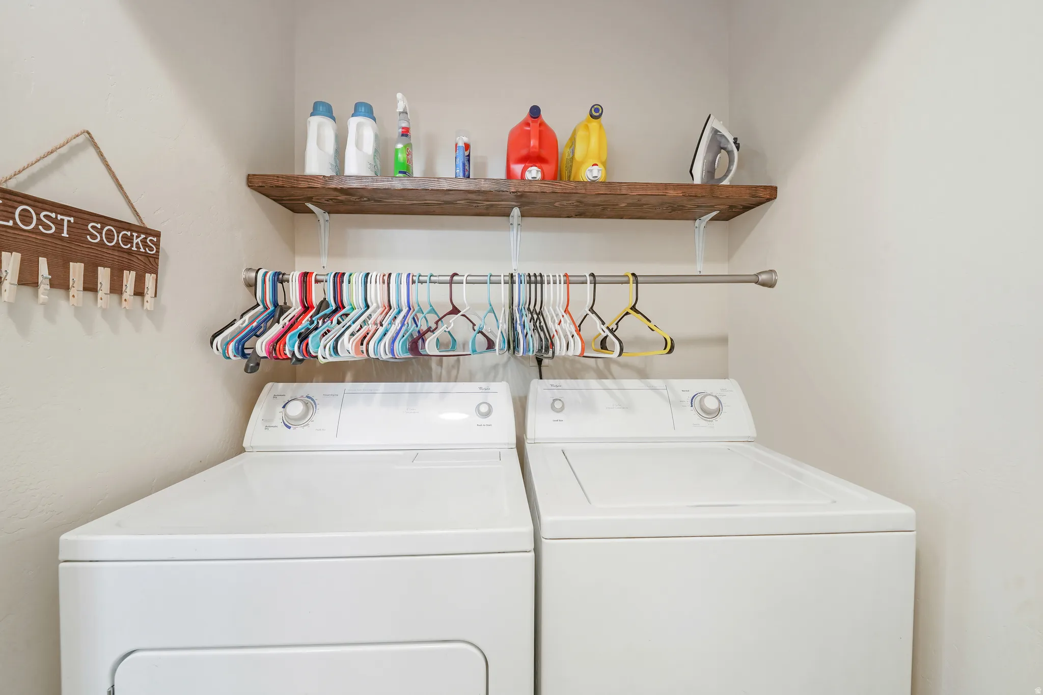 Dedicated laundry area featuring a wood-finish floating shelf, a metal hanging rod, and light-colored walls