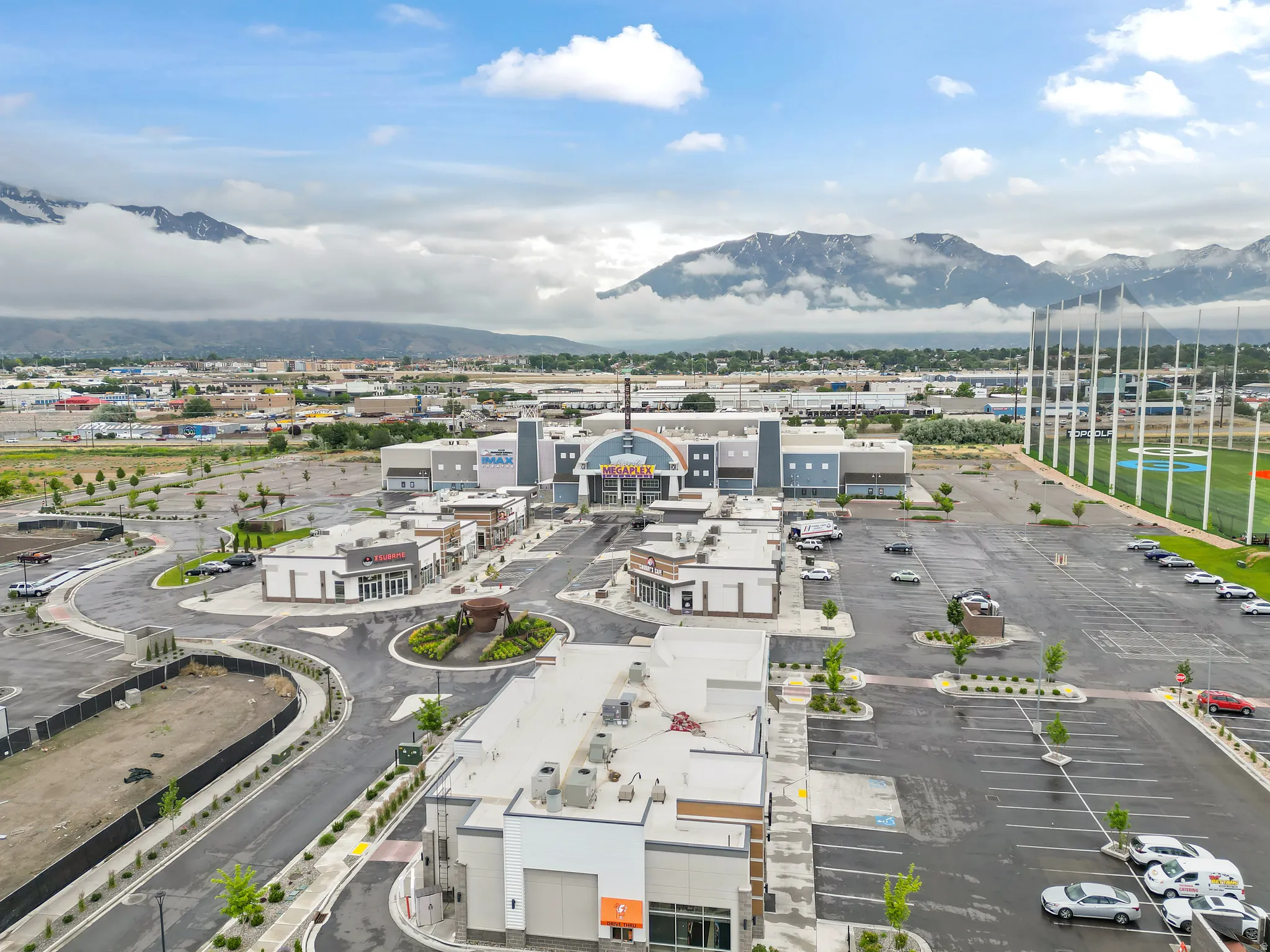 Expansive commercial complex featuring multiple retail establishments, ample parking facilities, and an adjacent recreational sports field