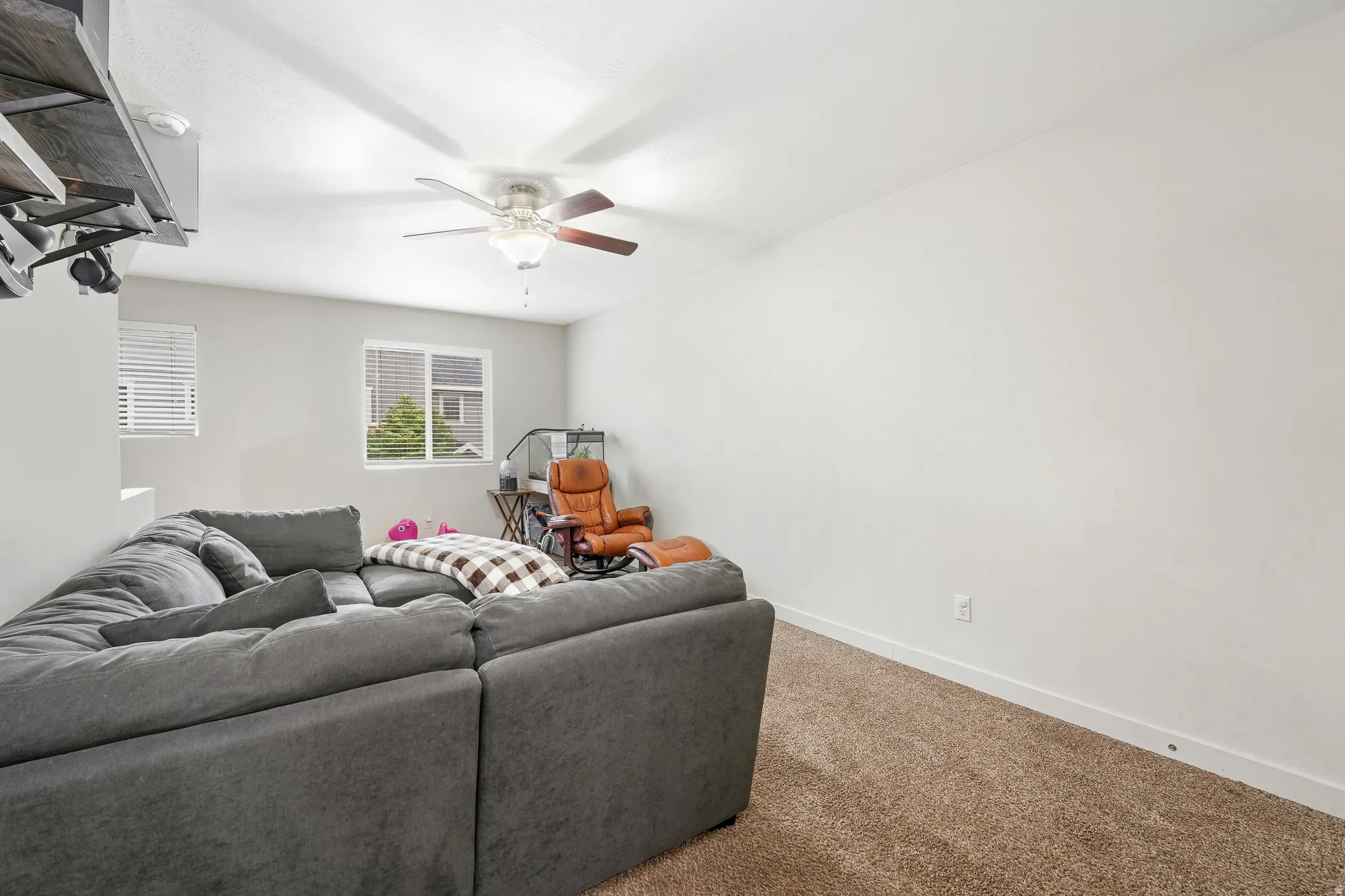 Carpeted room featuring a ceiling fan with light fixture, white walls, and a window with blinds