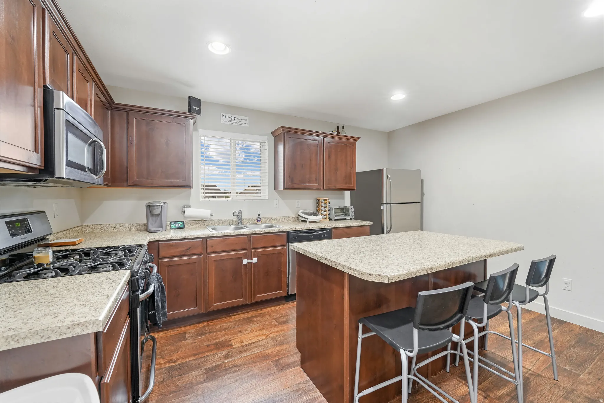 Kitchen featuring rich wood cabinetry, stainless steel appliances, a center island with countertop seating, granite-finish countertops, and wood-finish flooring