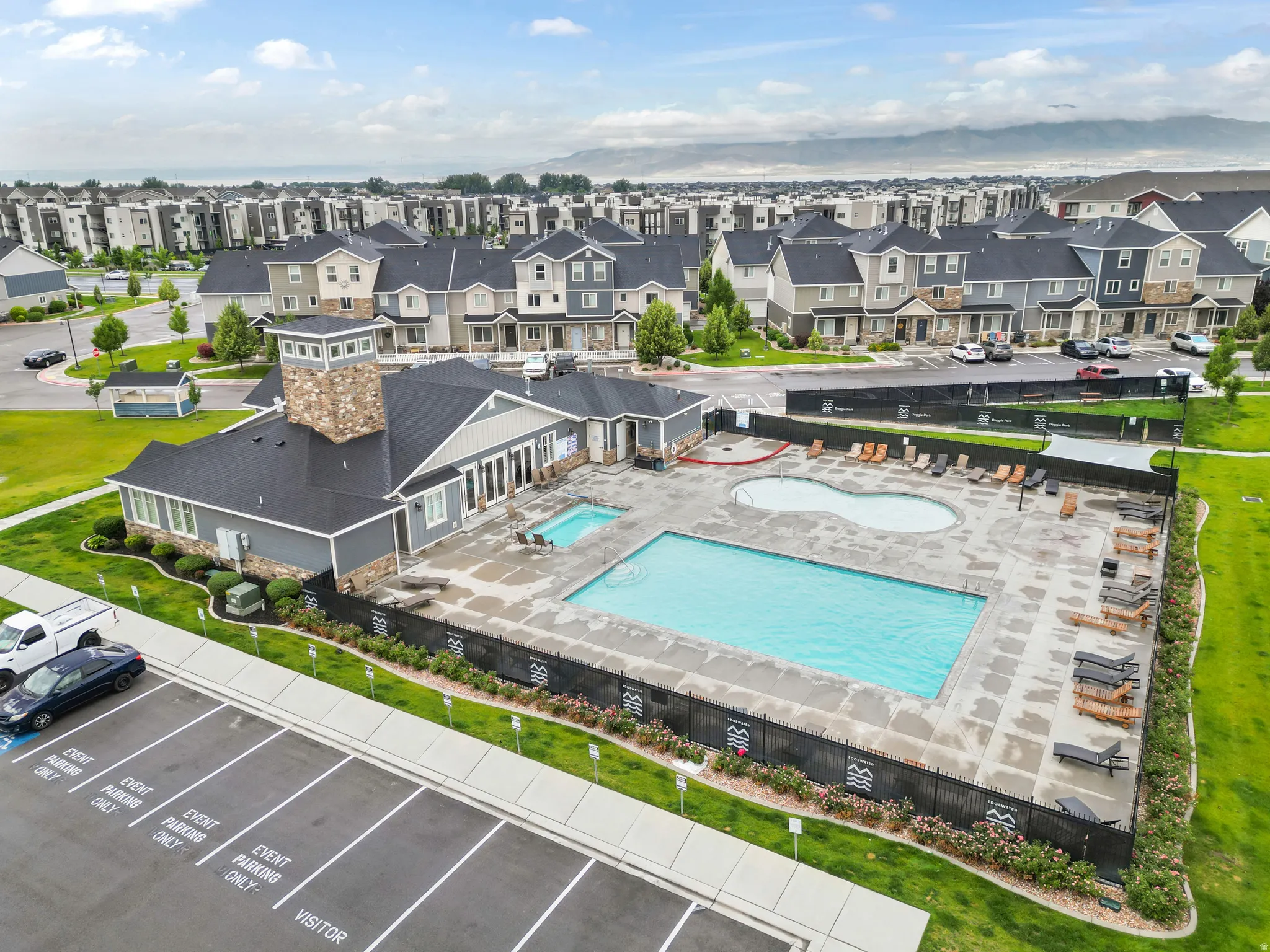 Community clubhouse featuring stone and siding exterior, two swimming pools, and an expansive paved pool deck