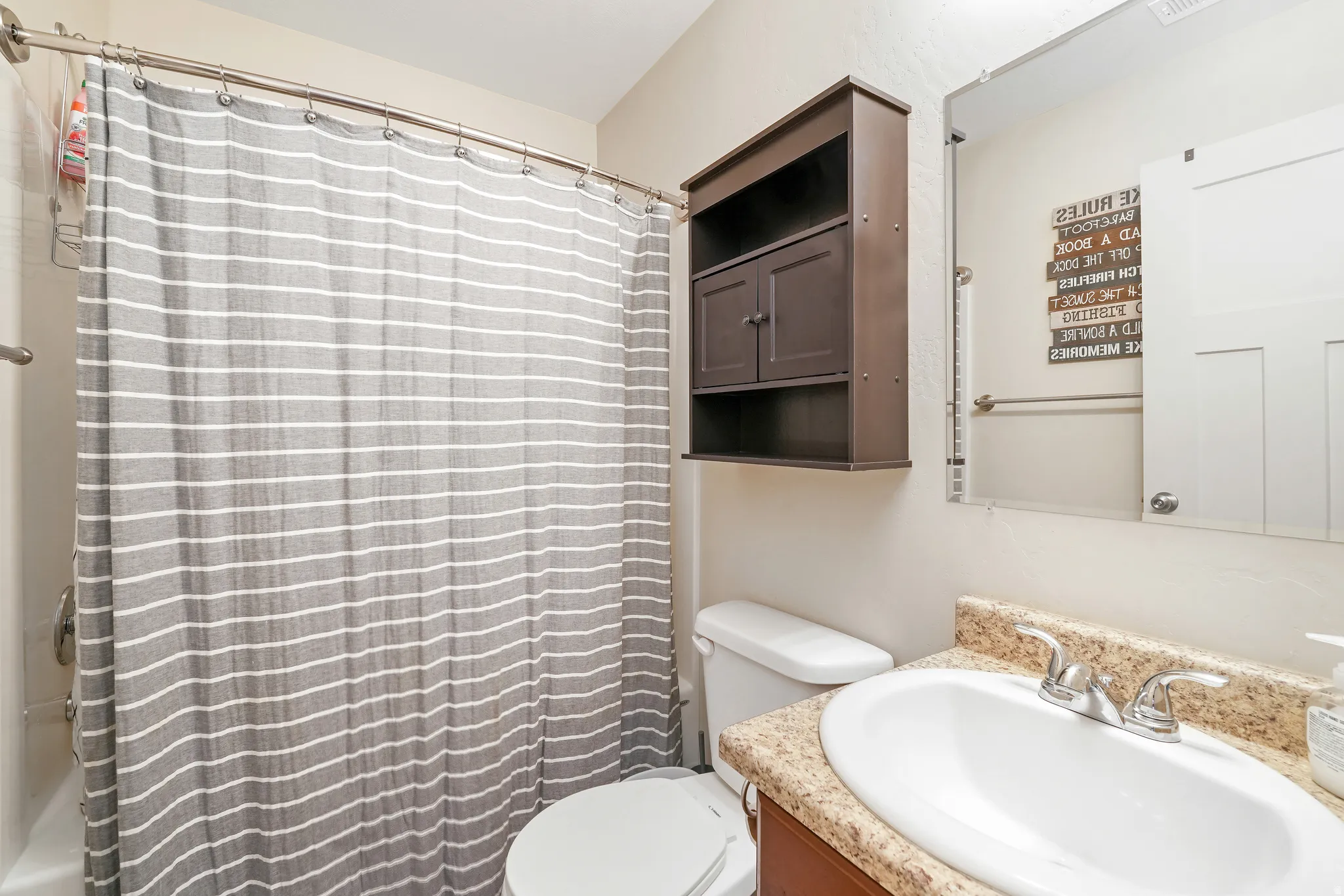 Full bathroom featuring a shower-tub combination with a curved shower rod, a wall-mounted storage cabinet, and a vanity with an integrated sink, dual-handle faucet, and granite-finish countertop