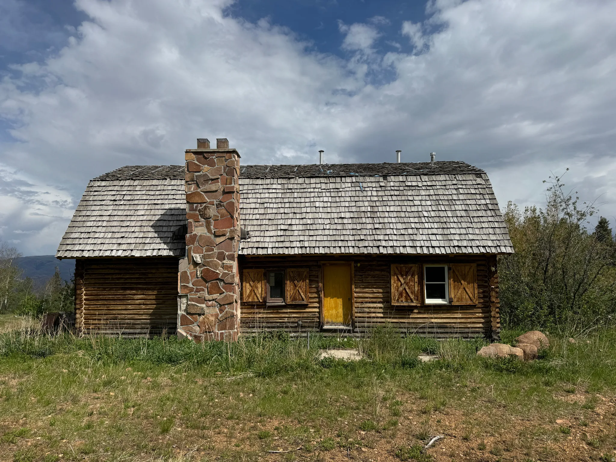 Rustic log cabin featuring a wood shake roof and a prominent stone chimney