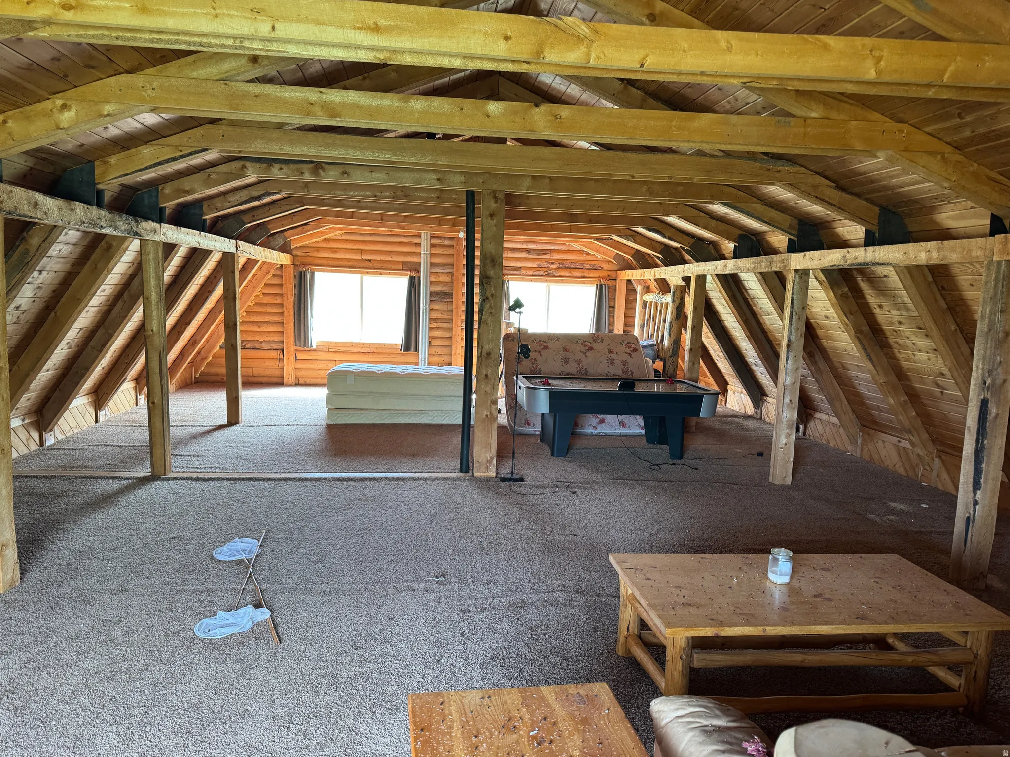 Expansive open space featuring exposed wood beam ceilings, wood-paneled walls, and carpet flooring
