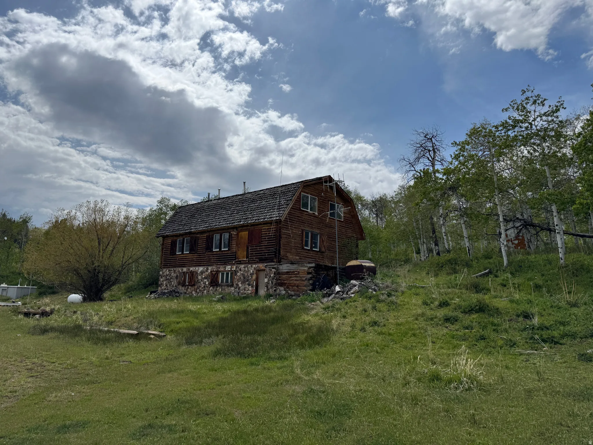 Log cabin structure featuring a gambrel roof and stone foundation