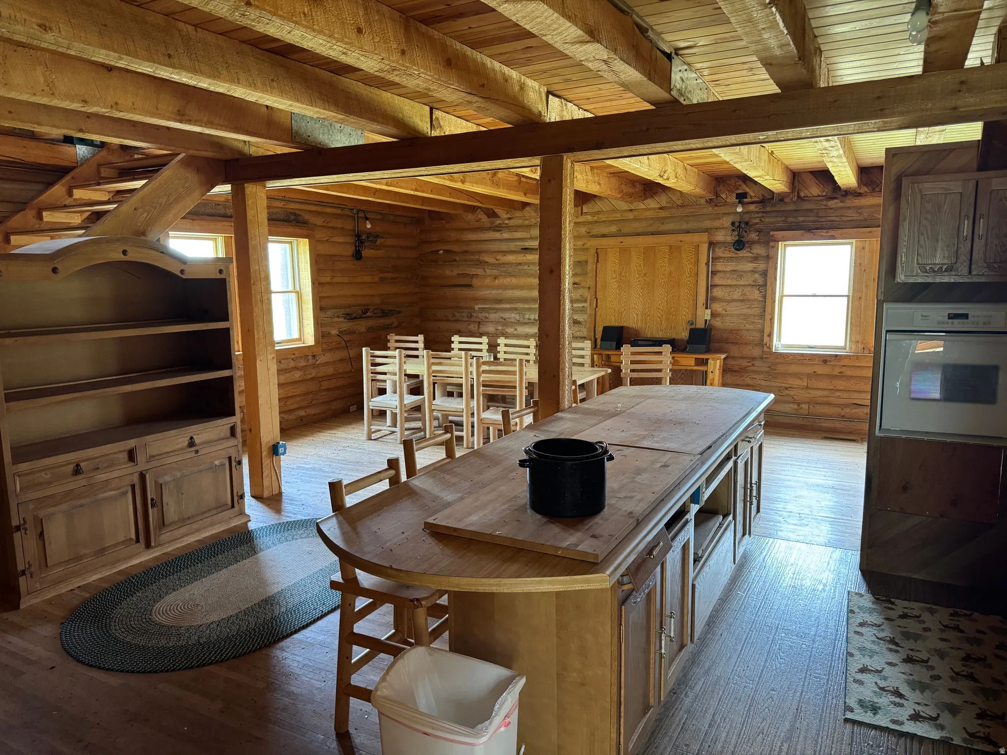 Open-concept space featuring exposed timber beams, wood-finish flooring, and horizontal log-style walls