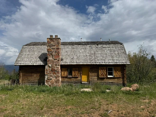Rustic log cabin featuring a wood shake roof and a prominent stone chimney