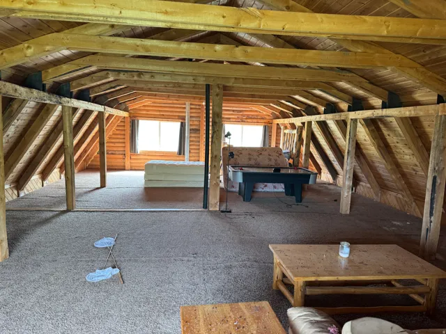 Expansive open space featuring exposed wood beam ceilings, wood-paneled walls, and carpet flooring