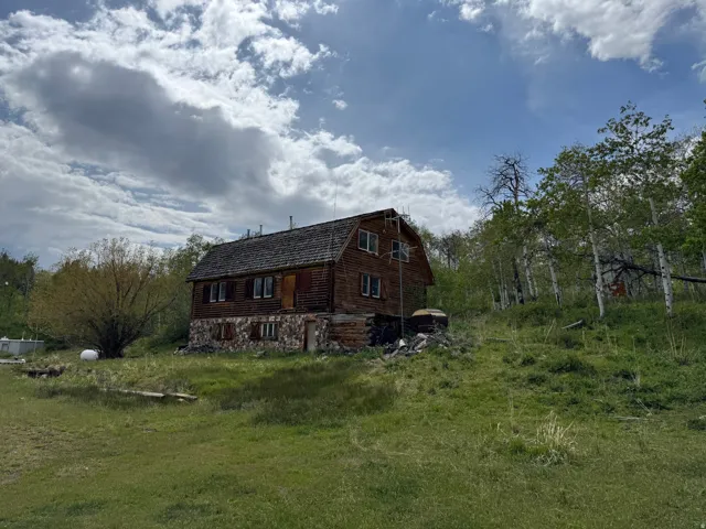 Log cabin structure featuring a gambrel roof and stone foundation