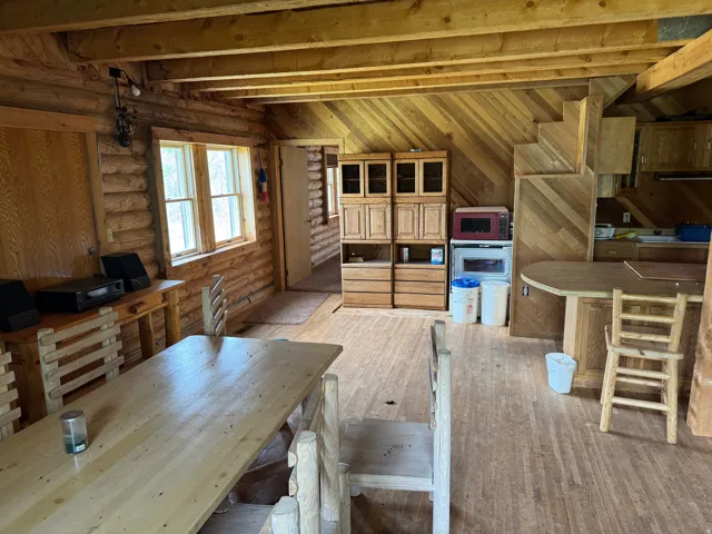 Interior showcasing log construction walls, exposed wood beams, wood-finish flooring, built-in wood cabinetry with glass fronts, and a wood-paneled staircase
