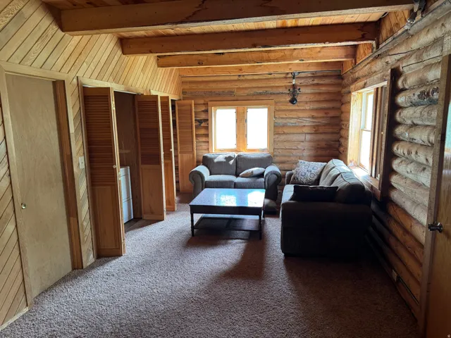 Living space featuring exposed log walls, a vaulted wood-paneled ceiling with exposed beams, and light-toned carpeting