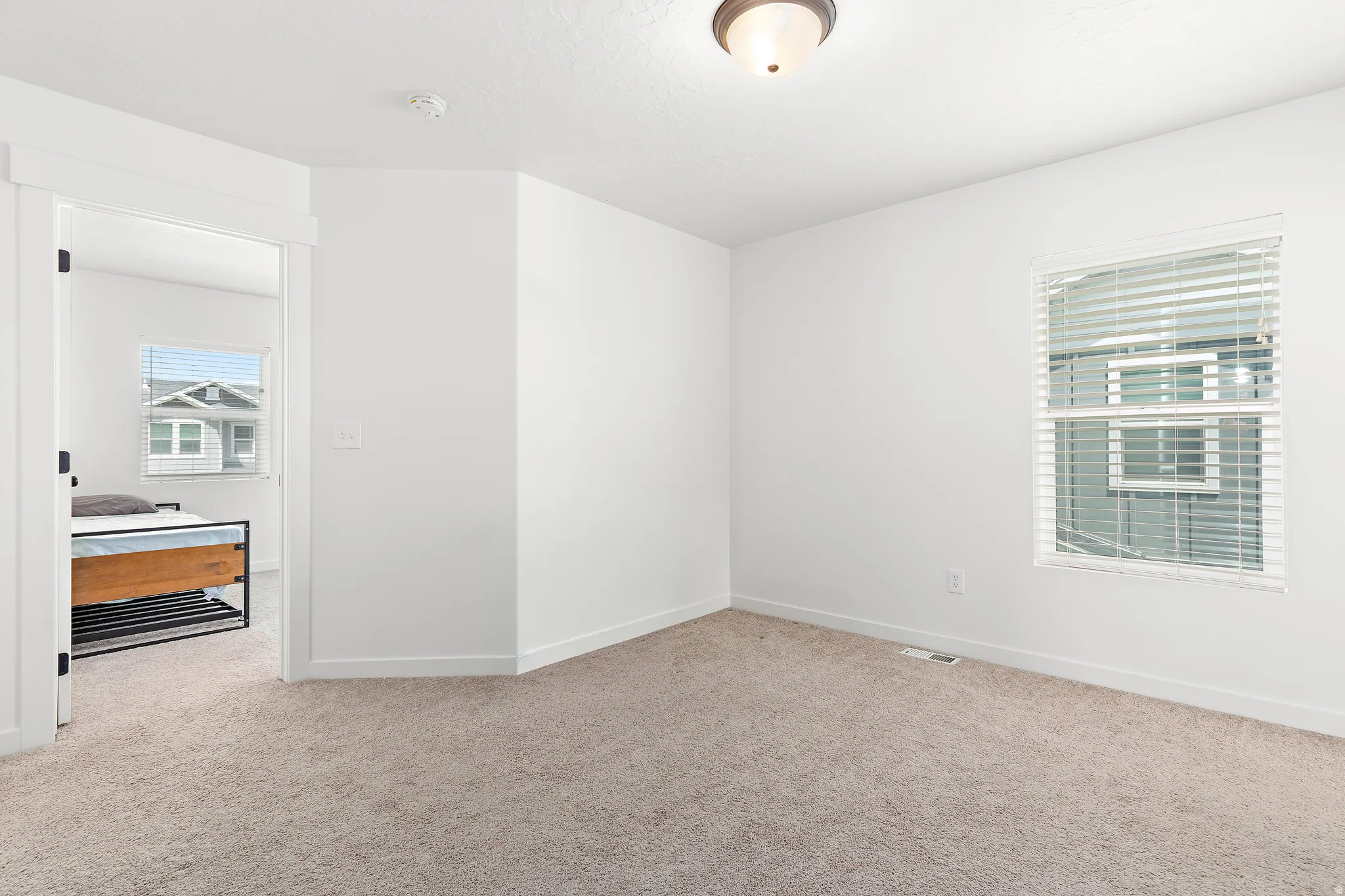 Carpeted room featuring white walls, a single window with blinds, and a semi-flush mount ceiling light