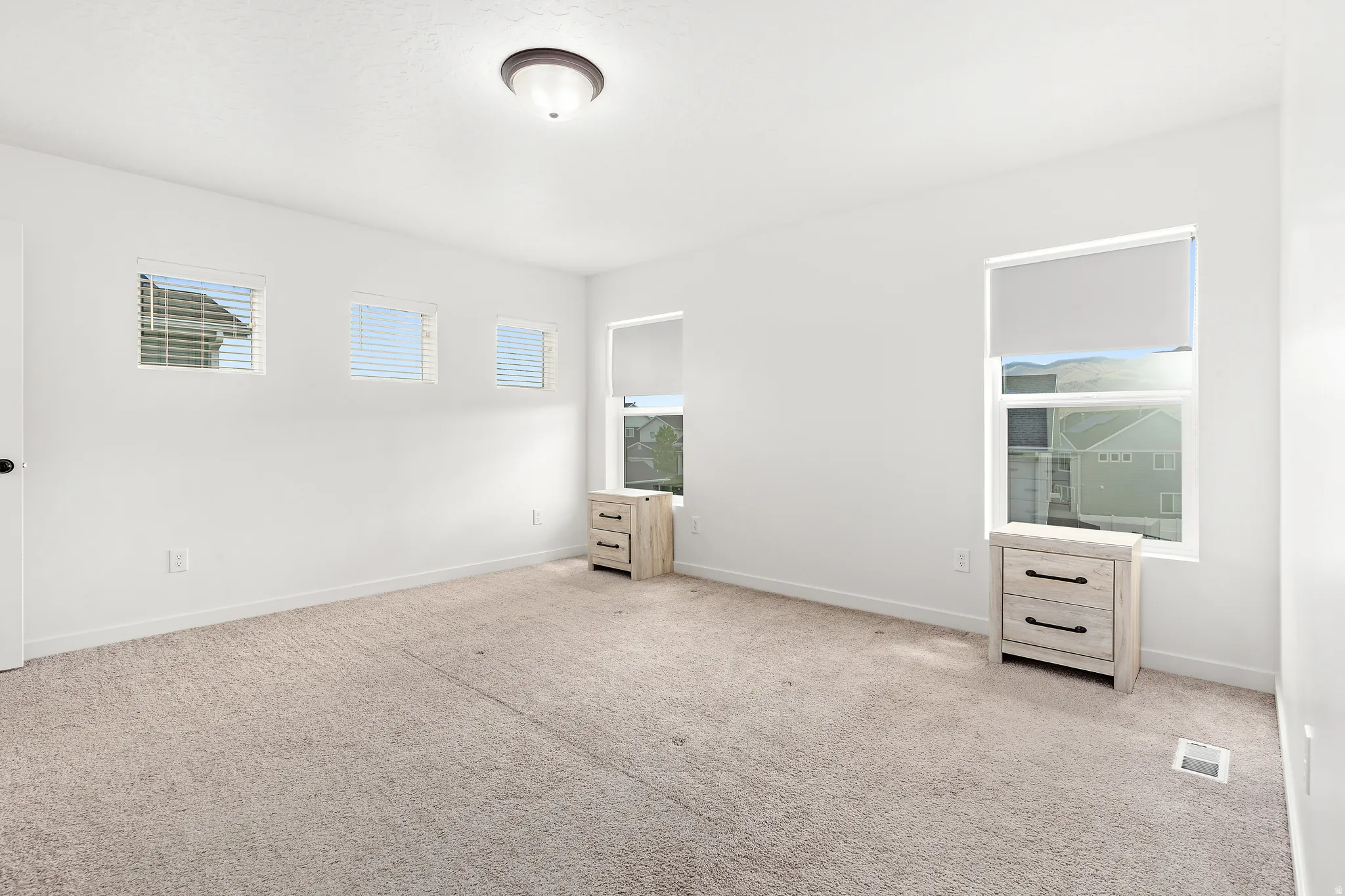 Carpeted room featuring multiple windows with blinds, a ceiling-mounted light fixture, and white walls