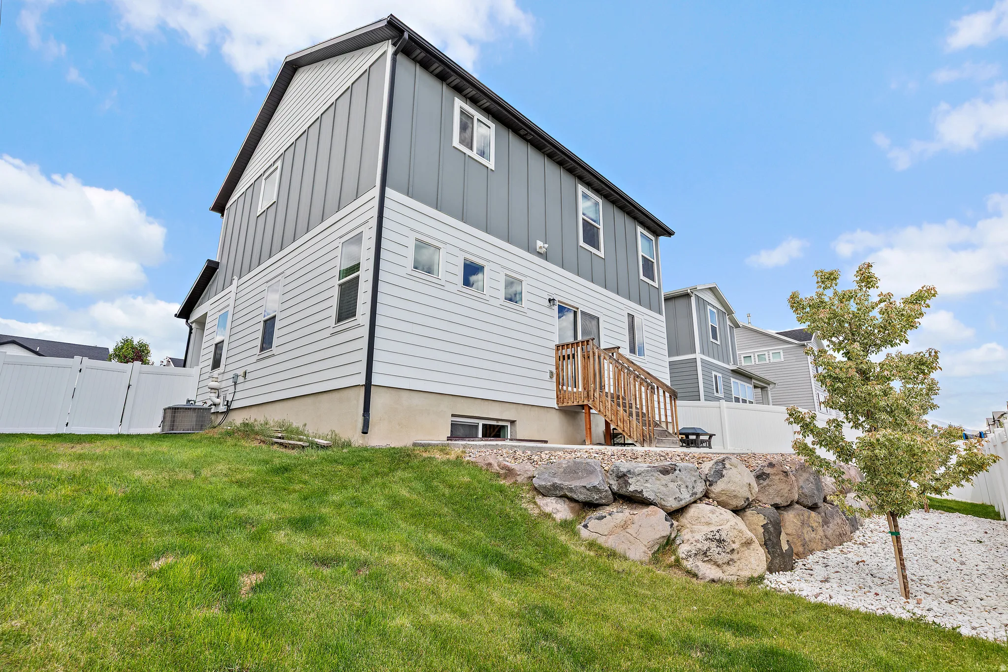Two-story residential exterior featuring gray vertical siding, white horizontal siding, a light-colored foundation, and a wooden deck with stairs