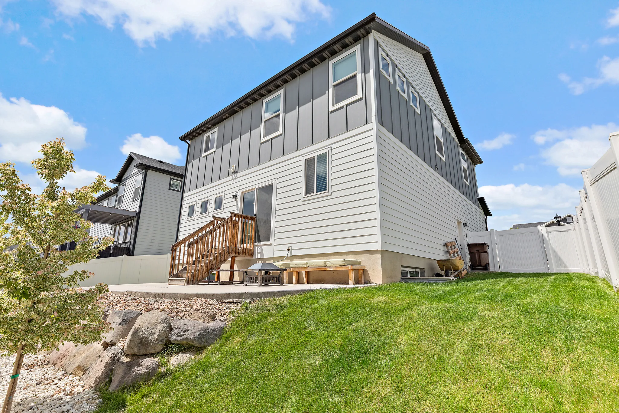 Rear exterior of a residence featuring multi-toned siding, a concrete patio, and a wood staircase with railing