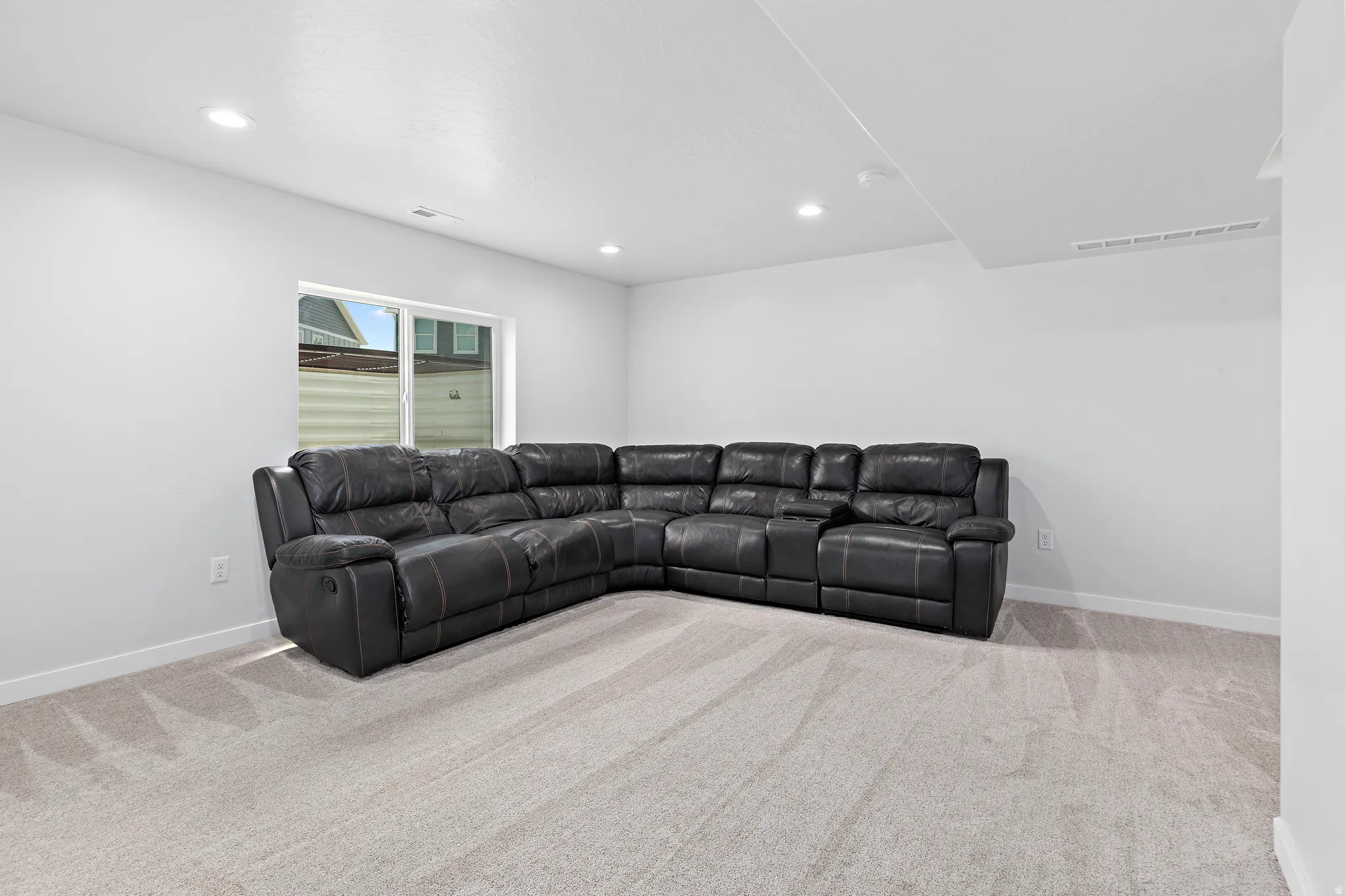 Spacious room featuring light gray carpeting, recessed ceiling lighting, a single window, and white baseboards