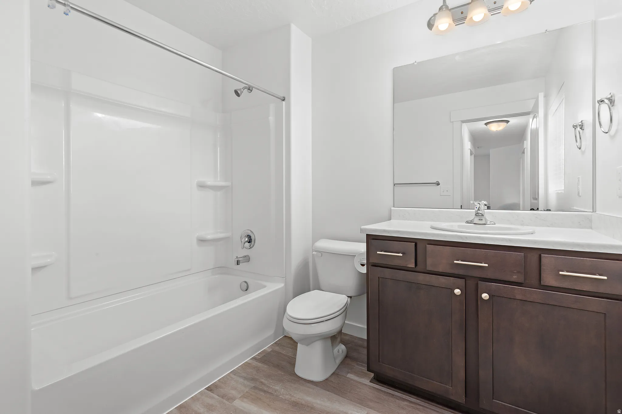 Full bathroom featuring a white tub/shower combination, dark wood-finish vanity with a light countertop, integrated sink, and wood-finish flooring