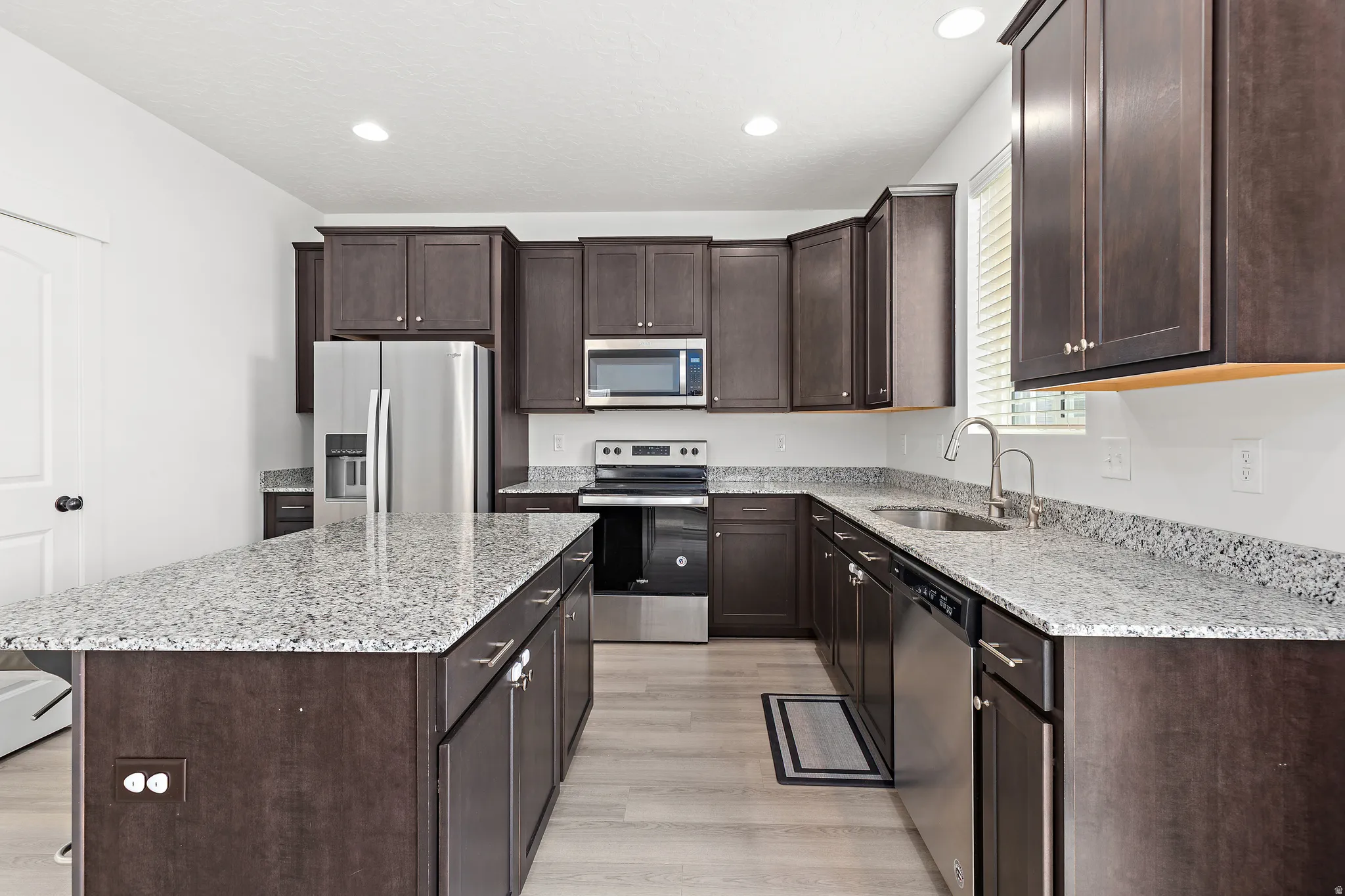 Kitchen featuring dark wood-finish cabinetry, light speckled countertops, stainless steel appliances, and wood-finish flooring