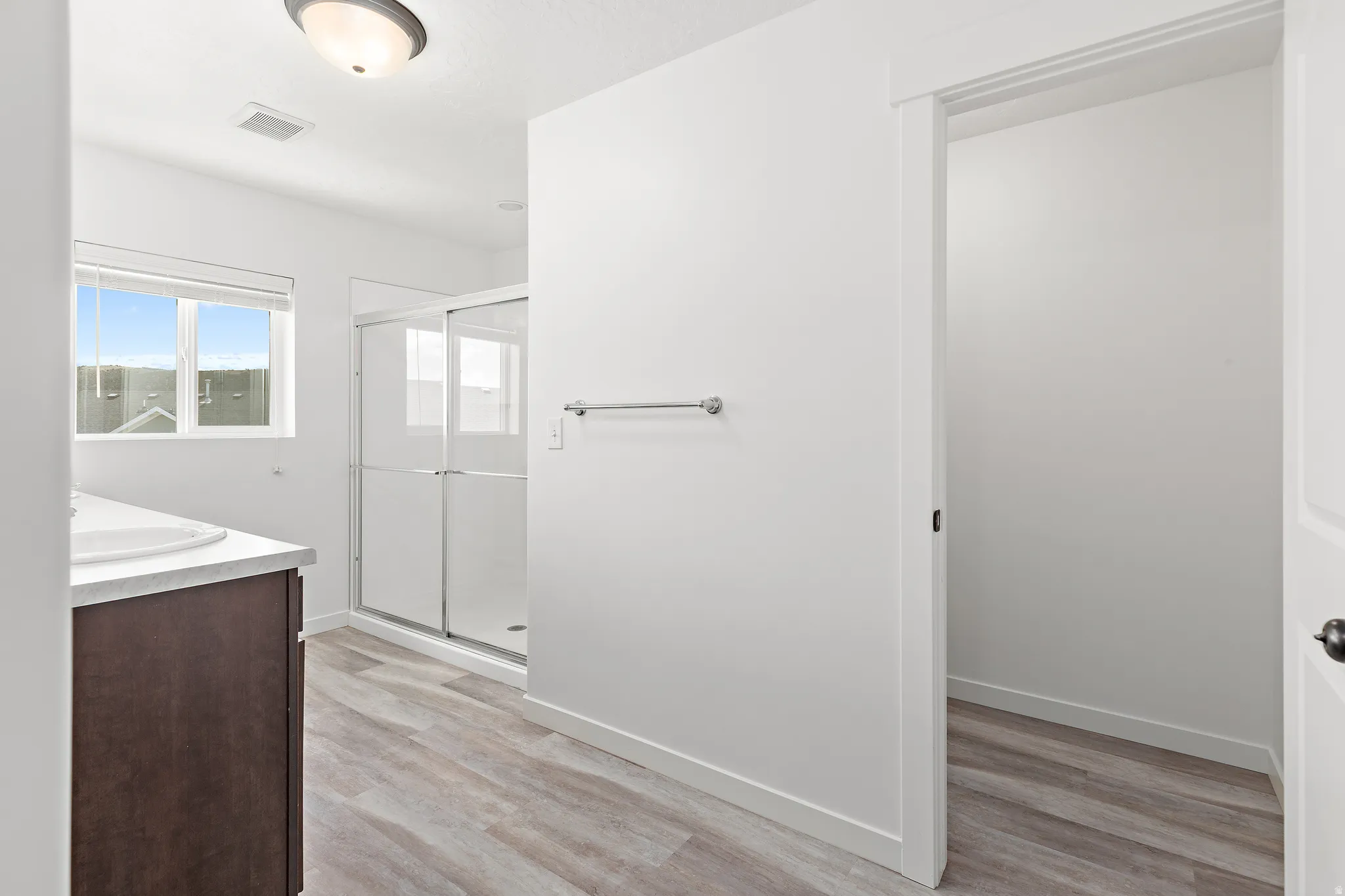 Bathroom featuring a sliding glass shower enclosure, wood-finish flooring, dark wood-tone vanity with a white countertop, and a window with horizontal blinds
