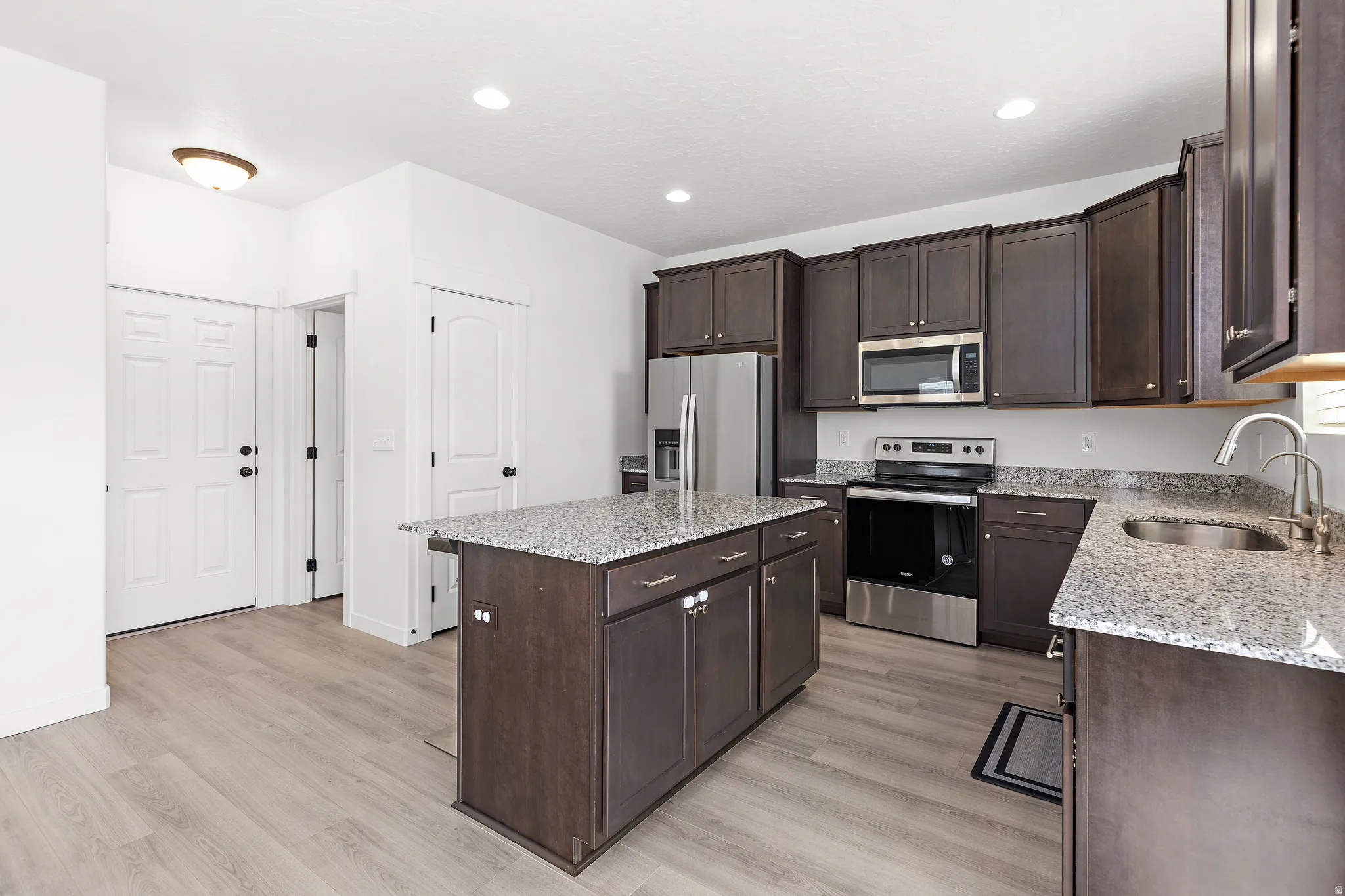 Kitchen featuring a central island, dark wood-finish cabinetry, stainless steel appliances, granite countertops, and wood-finish flooring