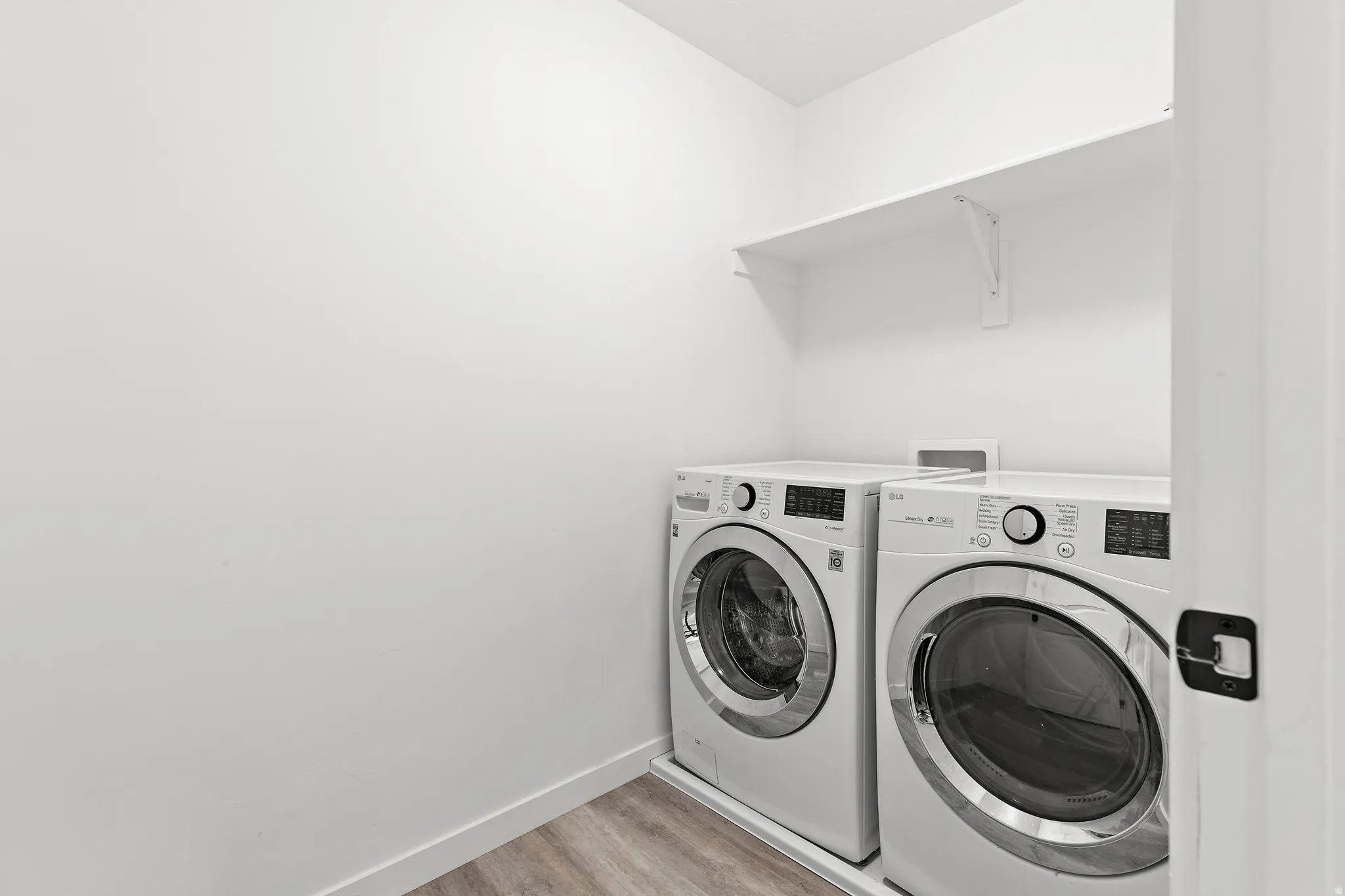 Dedicated laundry area with white walls, wood-finish flooring, and a single wall-mounted shelf