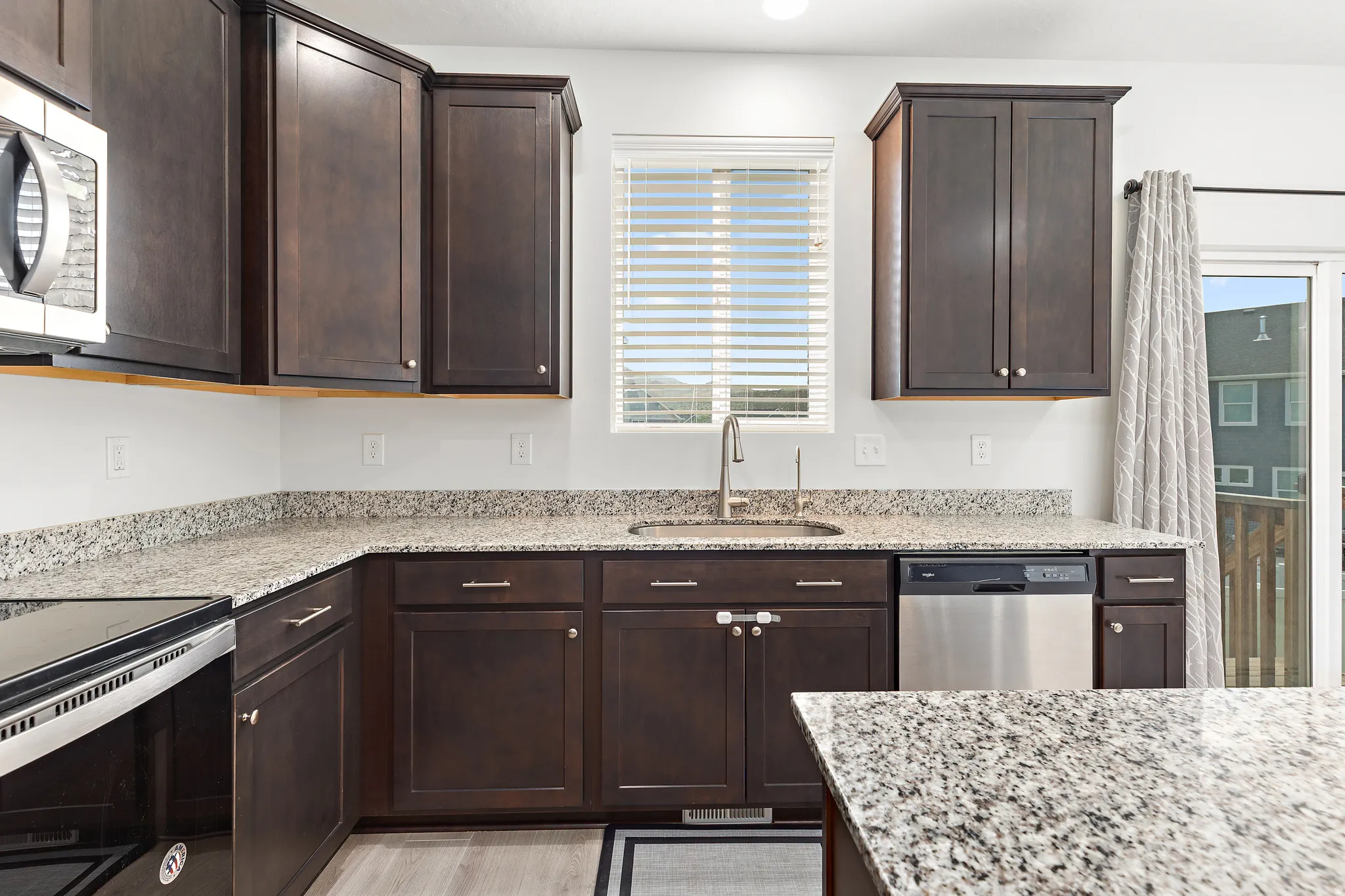Modern kitchen featuring dark wood cabinetry, light-toned granite countertops, and stainless steel appliances