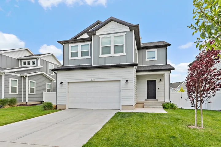 Modern two-story residence featuring a two-car garage, gray and white siding, a covered entry, and a manicured lawn