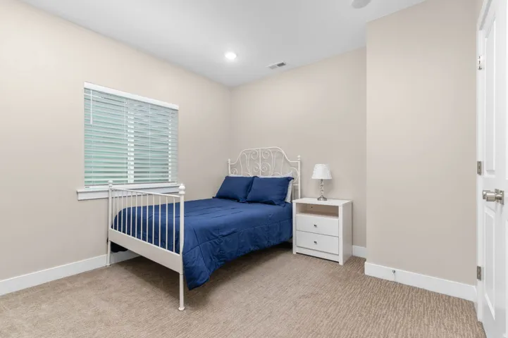 Bedroom featuring neutral wall paint, textured carpet flooring, a window with blinds, a white interior door, and a recessed ceiling light