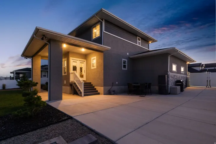 Rear exterior featuring a covered patio, dual entry doors, multi-level stairs with handrails, and a large concrete pad