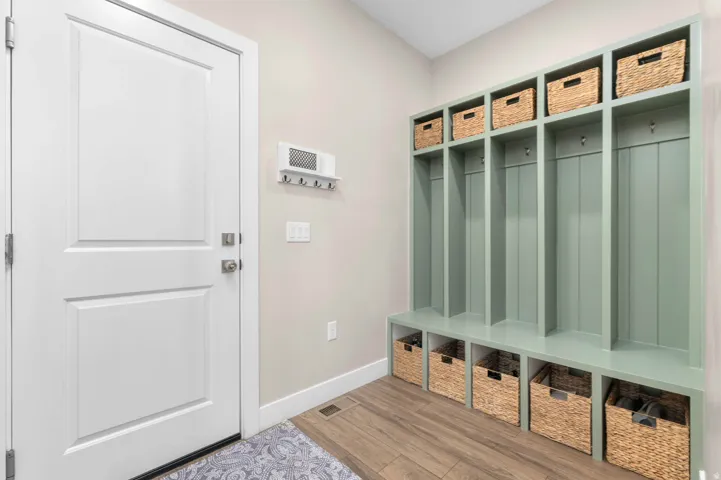 Mudroom featuring built-in green cabinetry with multiple storage cubbies, integrated bench seating, and overhead shelving