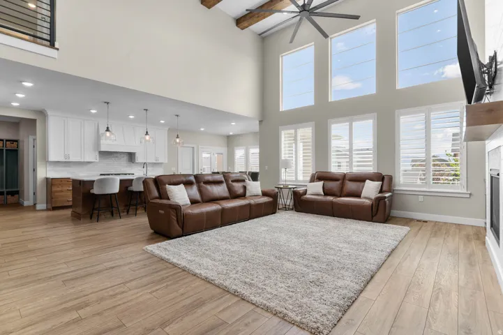 Open-concept living area featuring a two-story ceiling with exposed beams, wood-finish flooring, and a contemporary ceiling fan