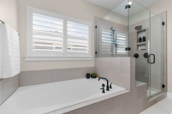Corner soaking tub with matte black fixtures, set within a tiled surround