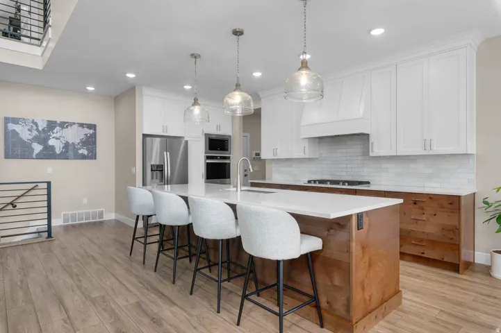 Kitchen featuring a substantial island with seating, pendant lighting, wood-finish flooring, white upper cabinetry, and stainless steel appliances