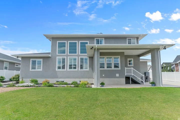 Expansive rear exterior featuring a covered patio, staircase, multiple windows, and a manicured lawn