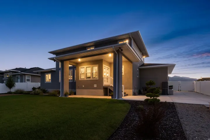 Modern exterior featuring a covered patio, expansive lawn, concrete patio area, and white vinyl fencing