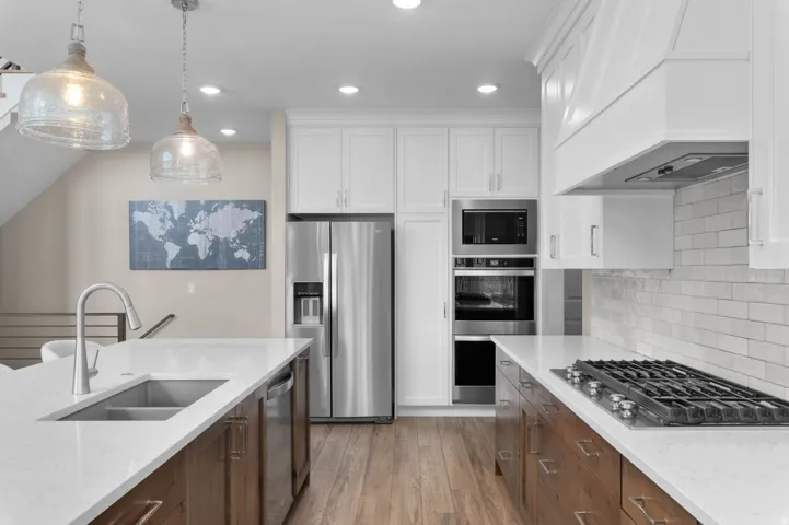 Gourmet kitchen featuring stainless steel appliances, a gas cooktop, white shaker cabinetry, wood-finish flooring, and pendant lighting