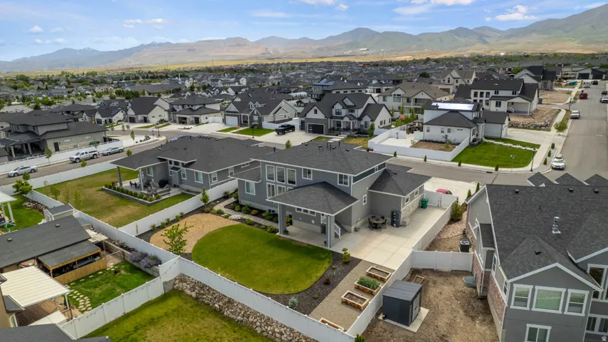 Modern two-story residence with a gray facade and dark roof, featuring a large concrete patio, an expansive lawn, and raised garden beds