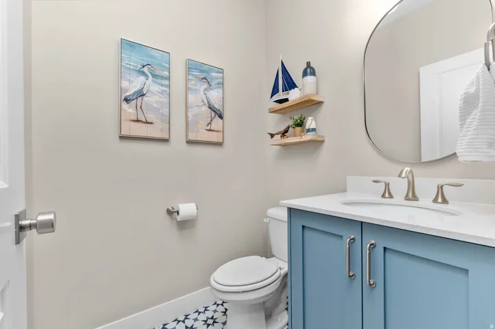 Powder room with a blue vanity featuring brushed nickel hardware, a white countertop, an undermount sink, and patterned floor tile