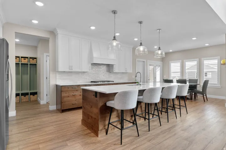 Gourmet kitchen featuring a substantial central island with seating, white shaker-style cabinetry, wood-finish flooring, recessed lighting, and clear glass pendant fixtures