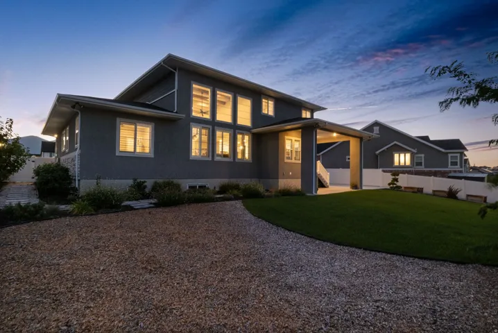 Contemporary two-story residence featuring a gravel driveway, expansive green lawn, and a covered patio area