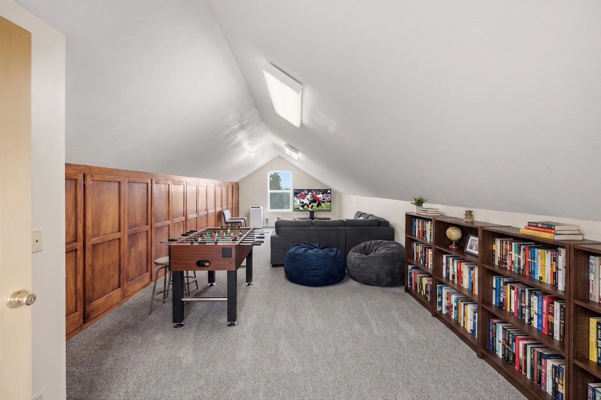 Spacious bonus room featuring vaulted ceilings, skylights, wood-panel accent wall, and built-in shelving