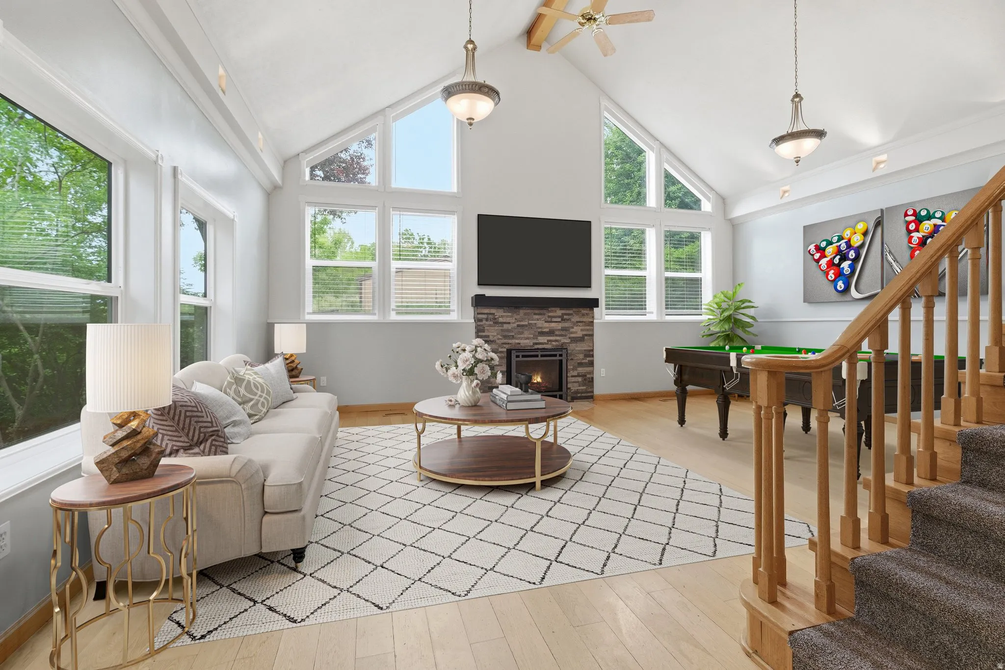 Vaulted ceiling living space featuring a stone-clad fireplace, wood-finish flooring, and multiple windows