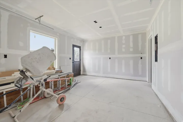 Drywall-finished interior space with a concrete floor, featuring a large window, a dark paneled door with glass inserts, and recessed ceiling lighting