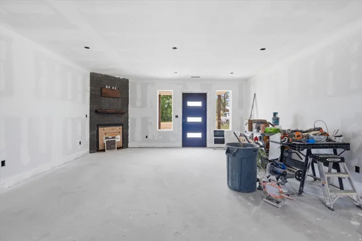 Spacious interior featuring a contemporary fireplace with a dark stone surround and wood mantels, recessed lighting, and a modern blue entry door with frosted glass panels