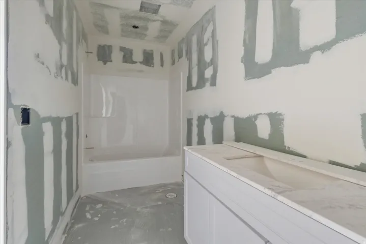 Bathroom under construction with a white bathtub/shower combination, a vanity with an integrated sink, and an installed countertop