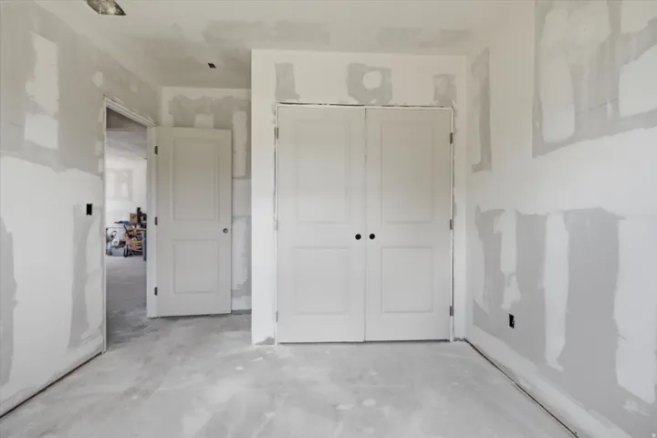 Interior construction space featuring unpainted drywall, a pair of white paneled doors with black hardware, and a single white paneled door