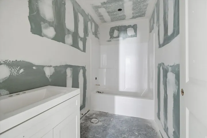 Bathroom under construction featuring a white vanity base with an integrated sink, a white tub and shower surround, and exposed drywall